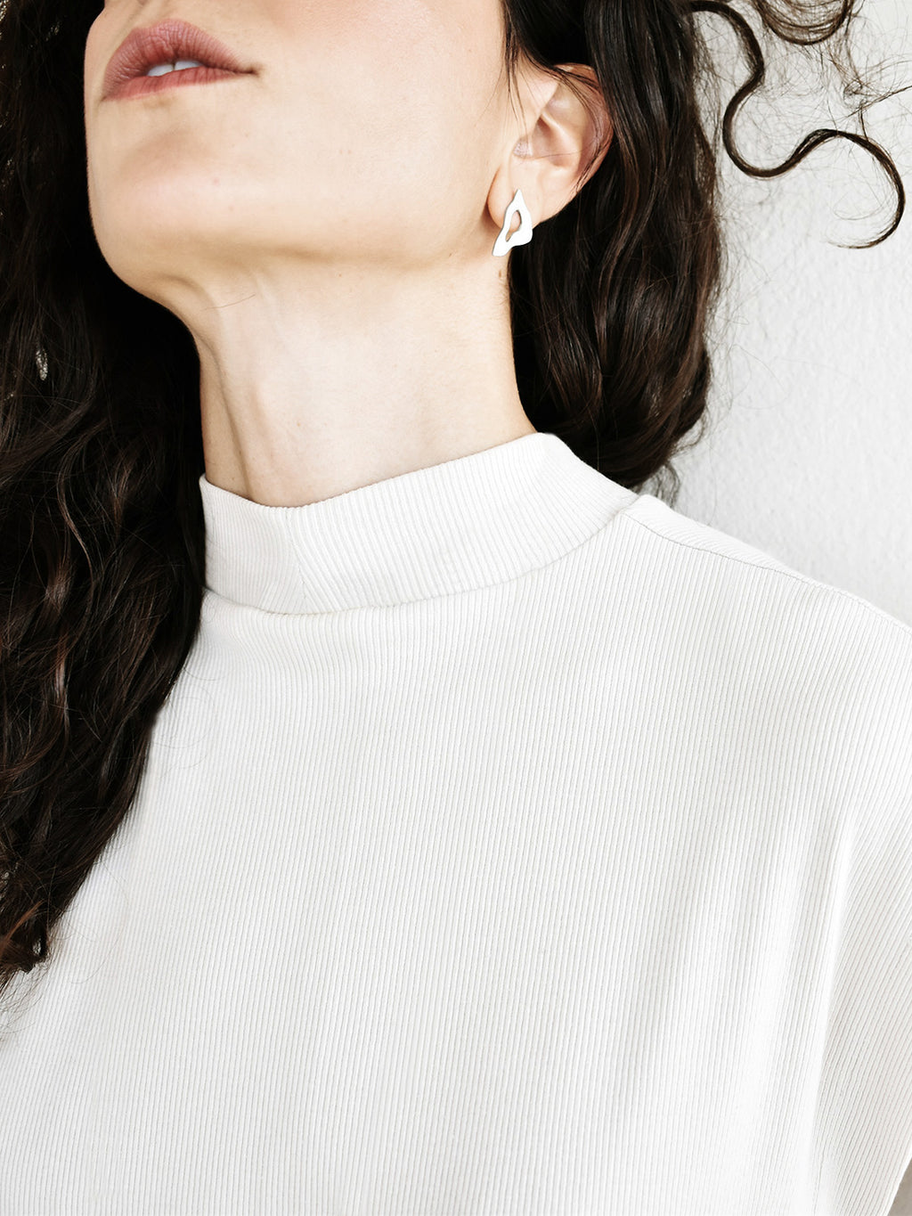 Woman wearing an organic-shaped silver stud earring with cutout centers in a white top