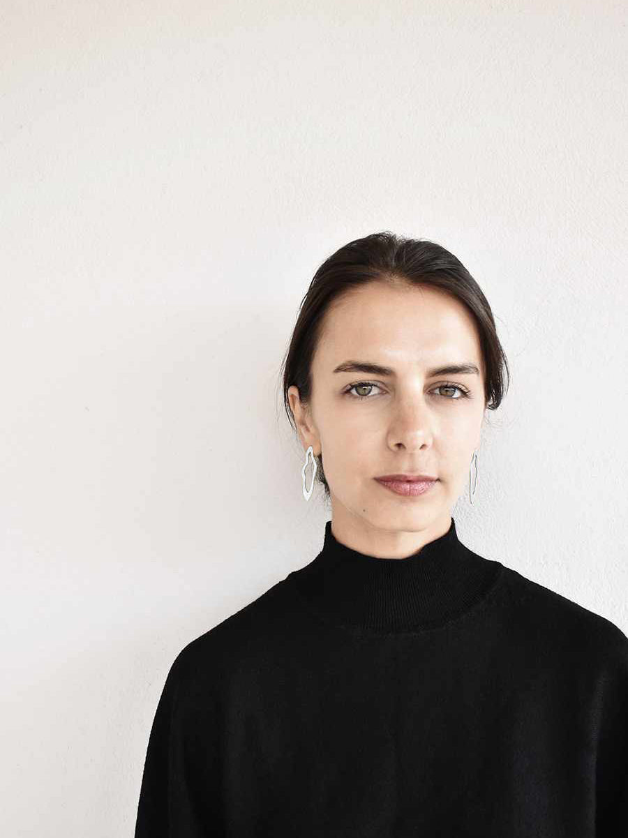 Woman wearing a pair of unique, organic-shaped silver stud earrings against a white background