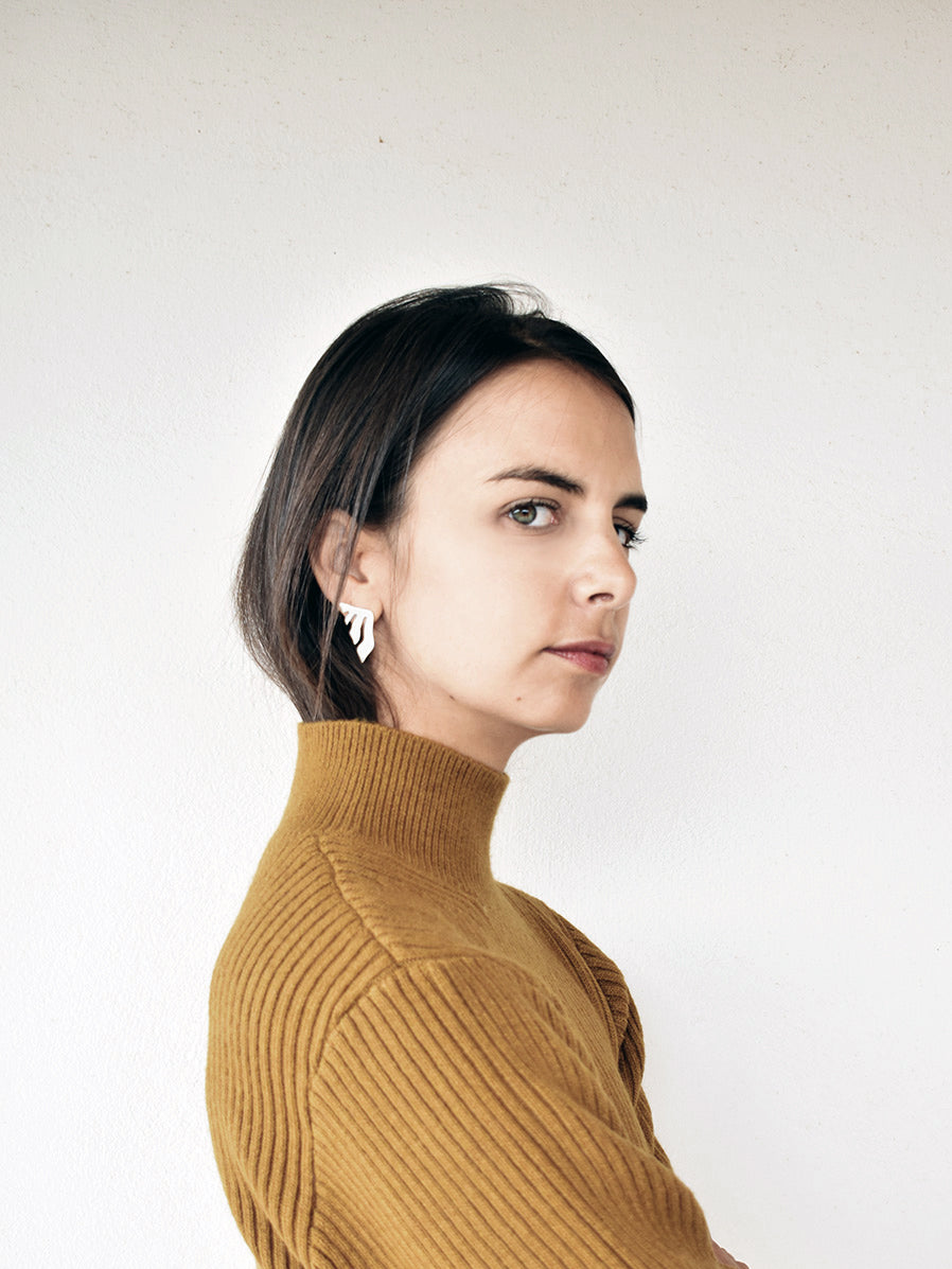 Woman wearing an organic-shaped silver stud earring with flowing cutouts in a mustard sweater