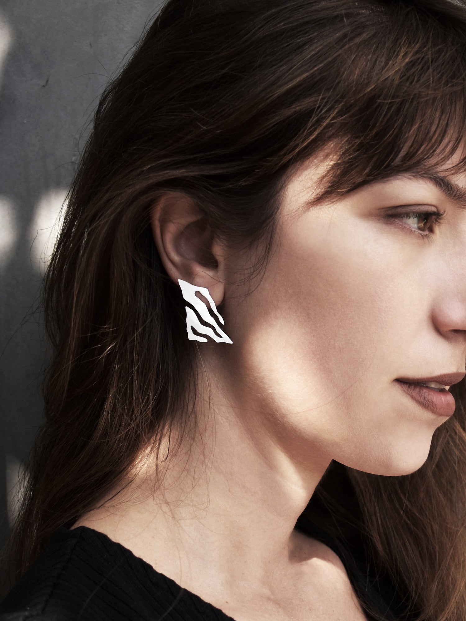 Close-up of a woman wearing an abstract-shaped silver stud earring with flowing cutouts