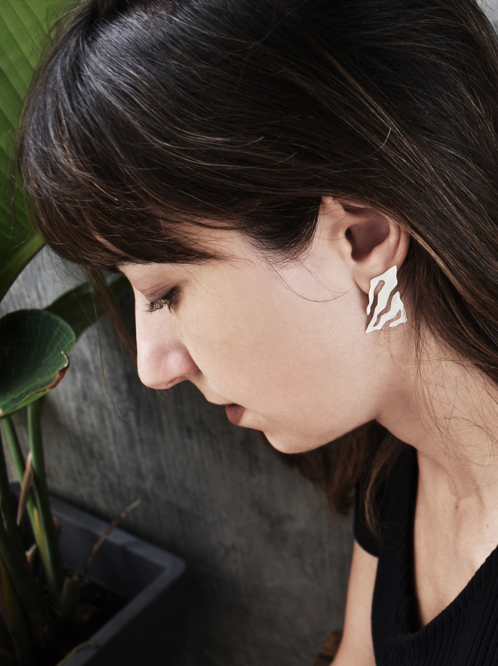 Close-up of a woman wearing an abstract-shaped silver stud earring with flowing cutouts 