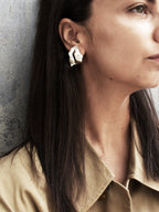 Woman wearing a sculptural silver stud earring with cutout centers 
