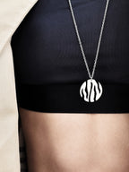 Round silver pendant with flowing cutouts and chain worn on a black top