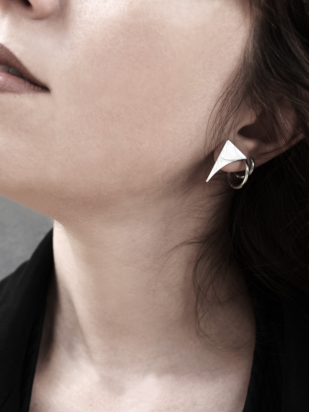 Close-up of a small curved triangular silver stud earring worn by a woman