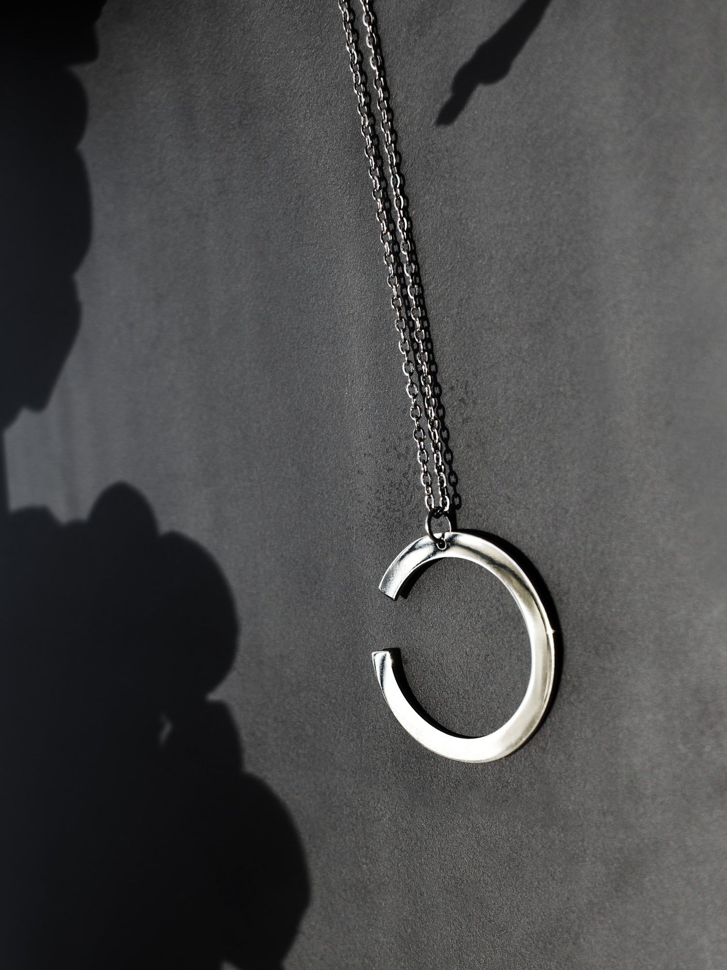 Silver crescent-shaped pendant with chain on a dark background