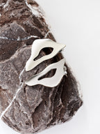 Pair of organic-shaped silver stud earrings with cutout centers on a textured stone