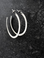 Pair of textured silver hoop earrings on a dark surface
