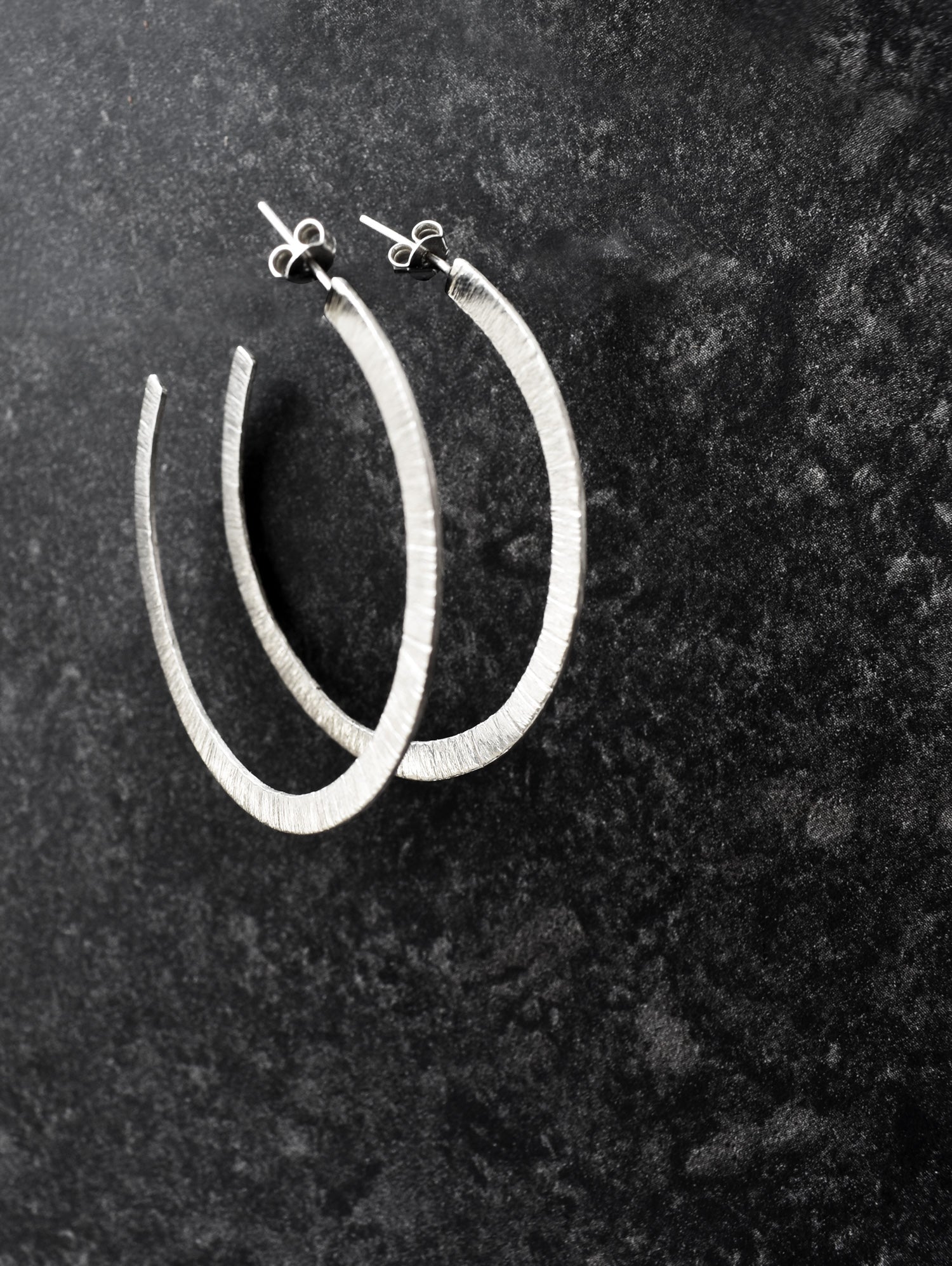 Pair of textured silver hoop earrings on a dark surface