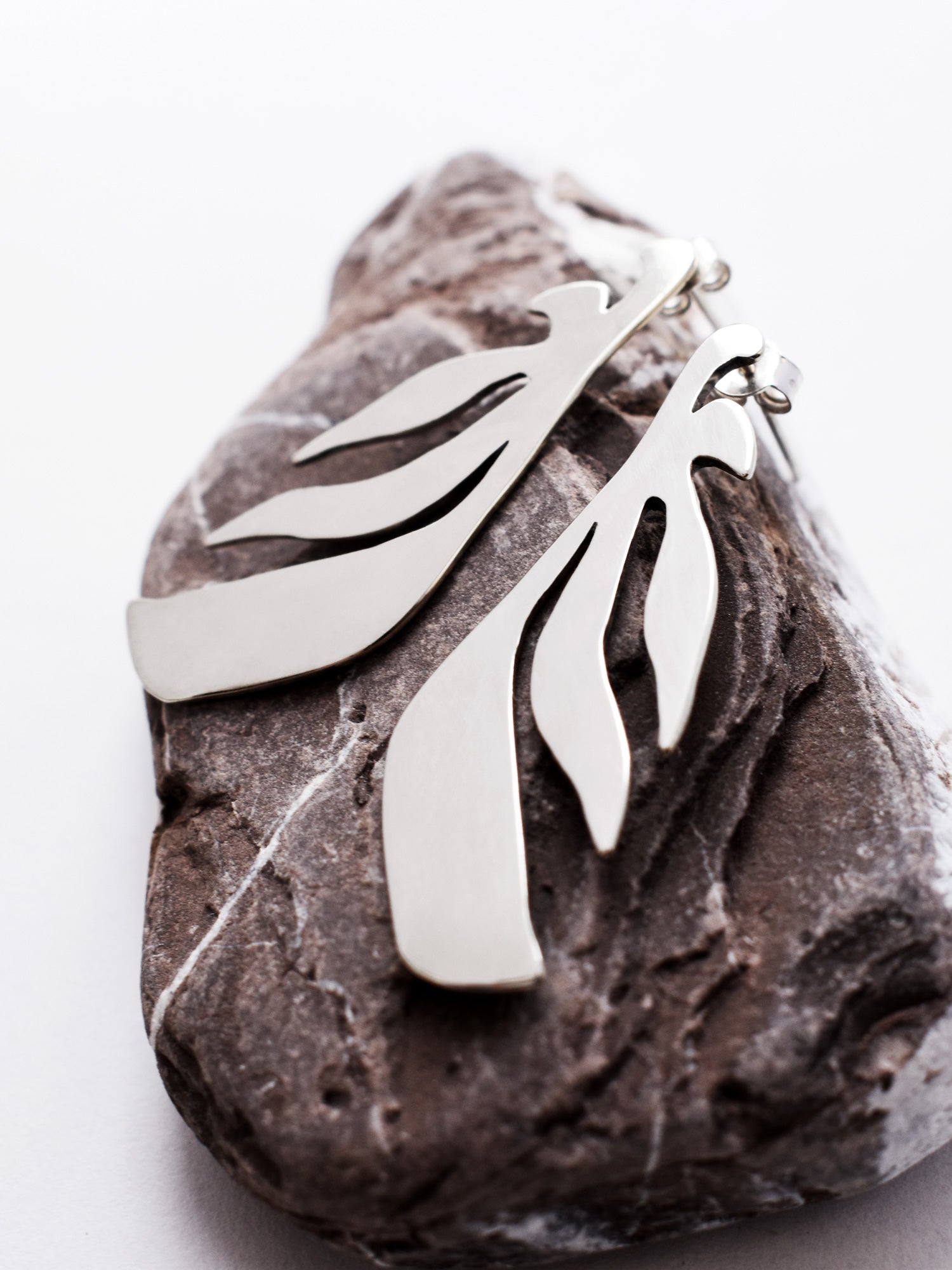 Pair of leaf-shaped silver stud earrings on a textured stone 