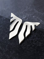 Pair of organic-shaped silver stud earrings with flowing cutouts on a dark textured surface