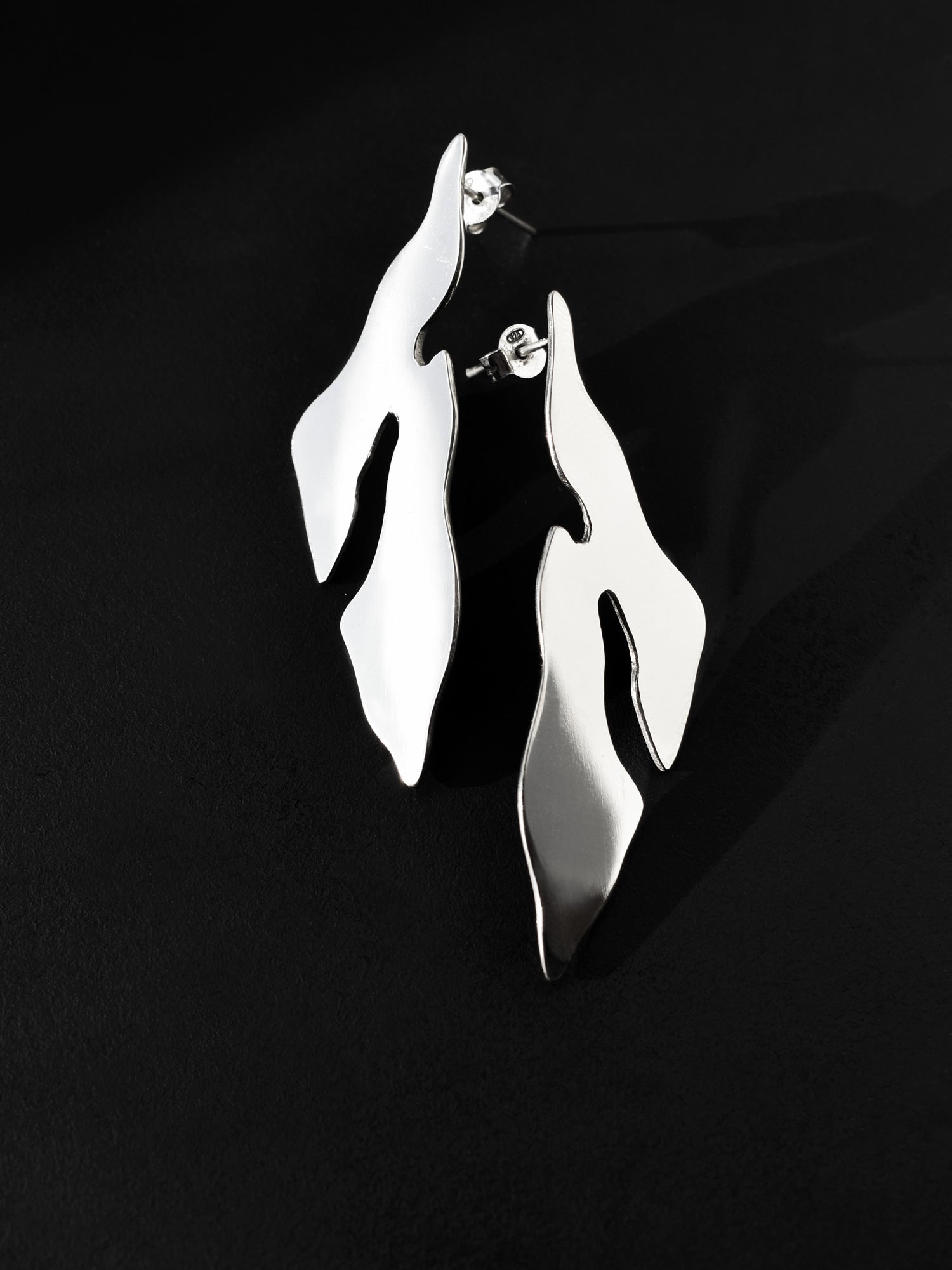 Pair of abstract-shaped silver stud earrings on a black background