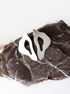 Pair of organic-shaped silver stud earrings with cutout centers on a textured stone
