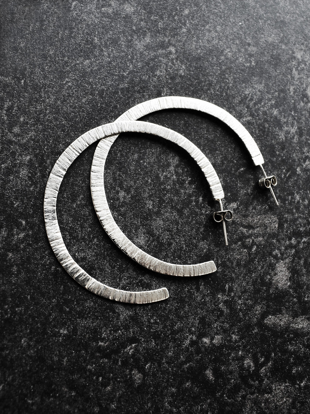 Pair of textured silver hoop earrings on a dark surface