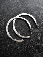 Pair of textured silver hoop earrings on a dark surface