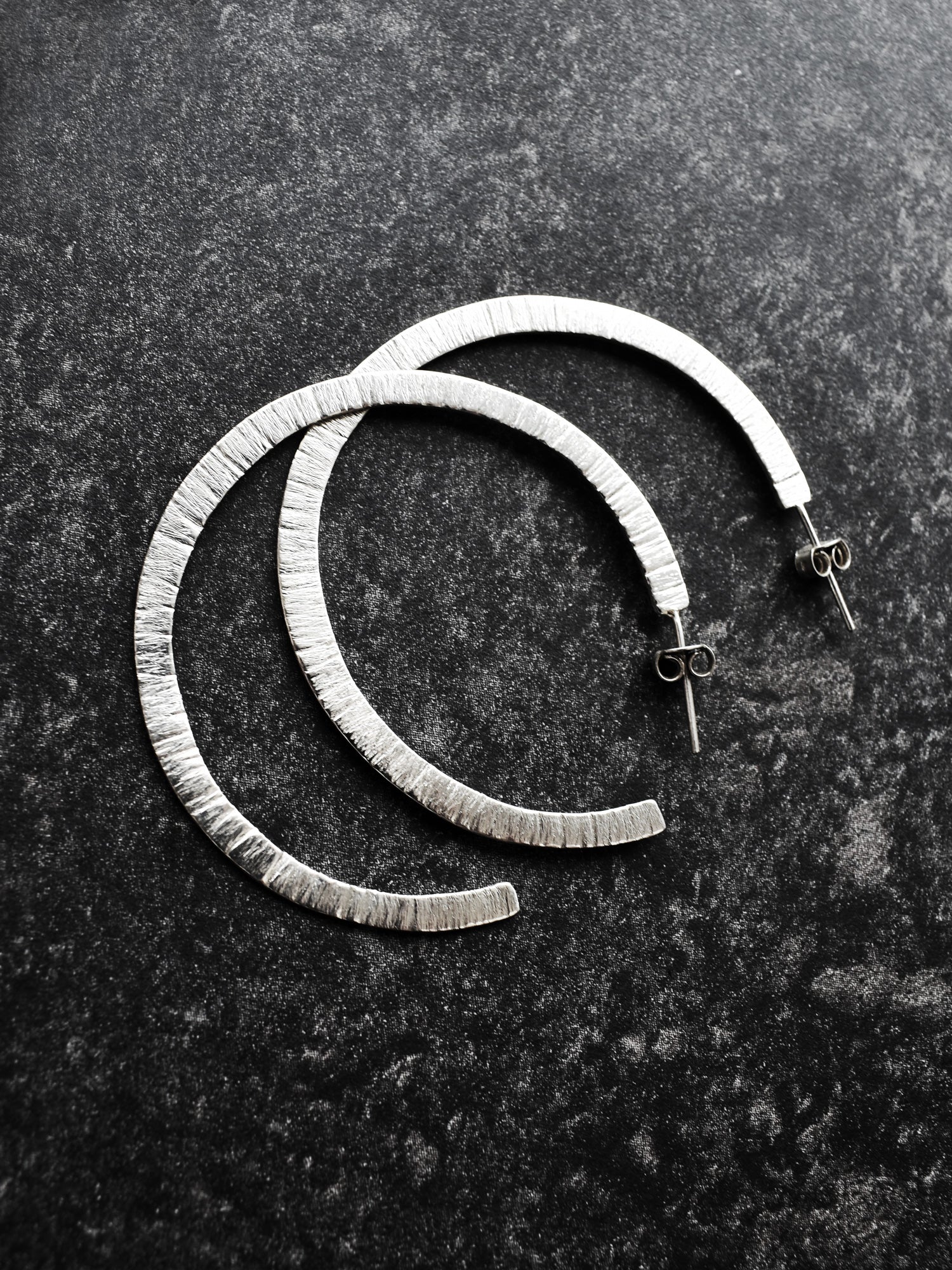 Pair of textured silver hoop earrings on a dark surface