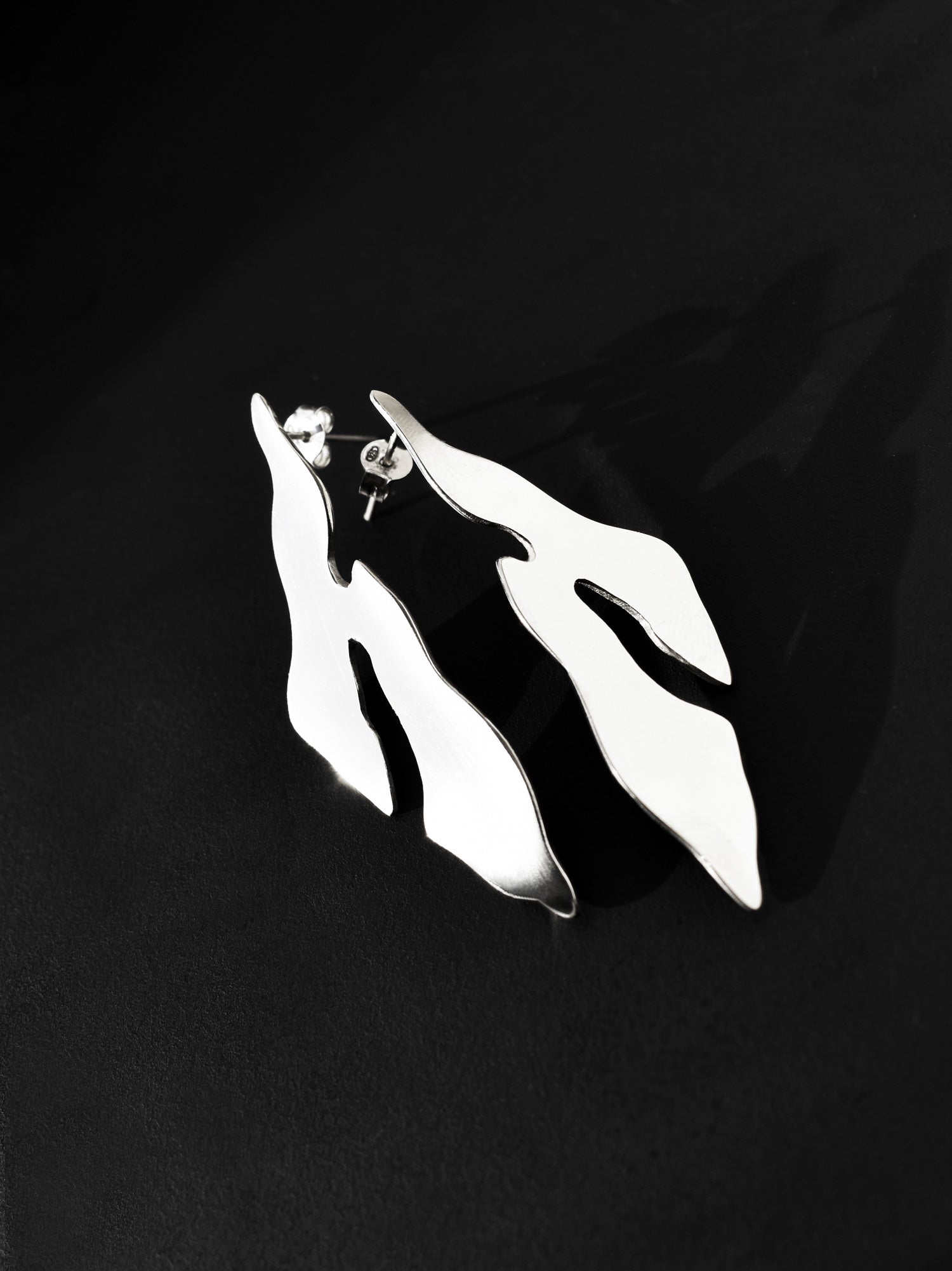 Pair of abstract-shaped silver stud earrings on a black background