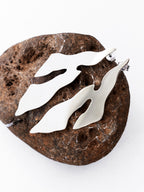 Pair of abstract-shaped silver stud earrings on a textured brown stone