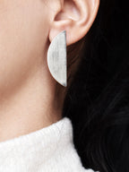 Close-up of a brushed silver semicircle stud earring on a woman