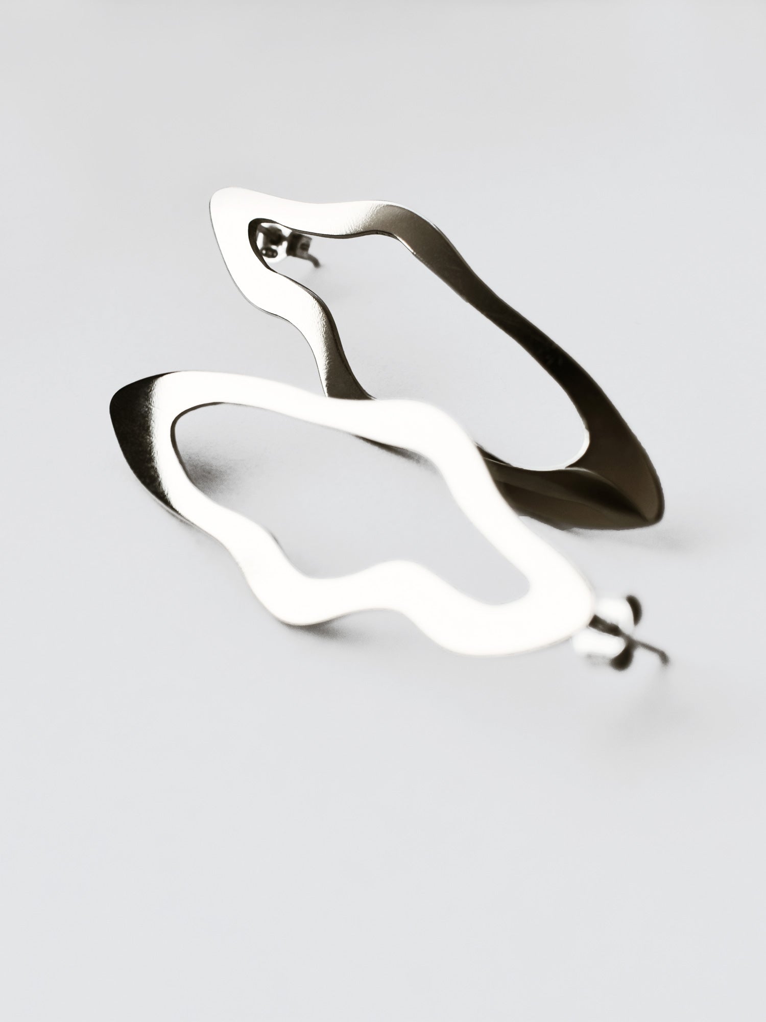 Close-up of a pair of unique, organic-shaped silver stud earrings on a light gray background