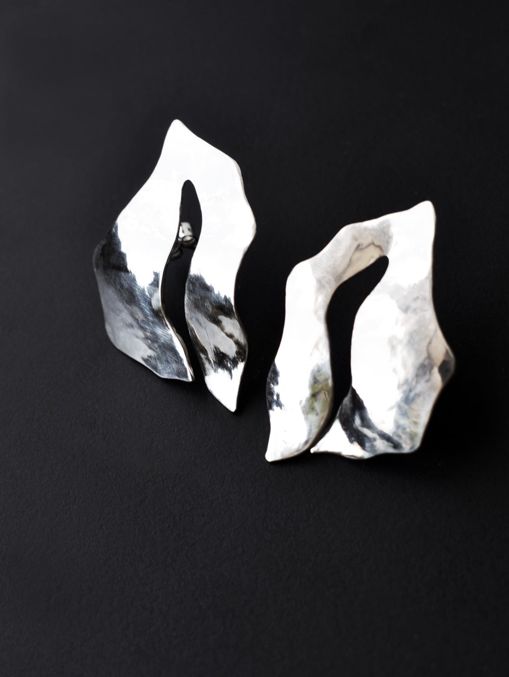 Pair of sculptural silver stud earrings with cutout centers on a black background