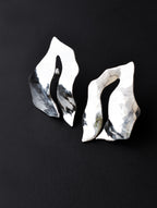 Pair of sculptural silver stud earrings with cutout centers on a black background