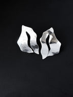 Pair of sculptural silver stud earrings with cutout centers on a black background