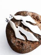 Pair of abstract-shaped silver stud earrings on a textured brown stone