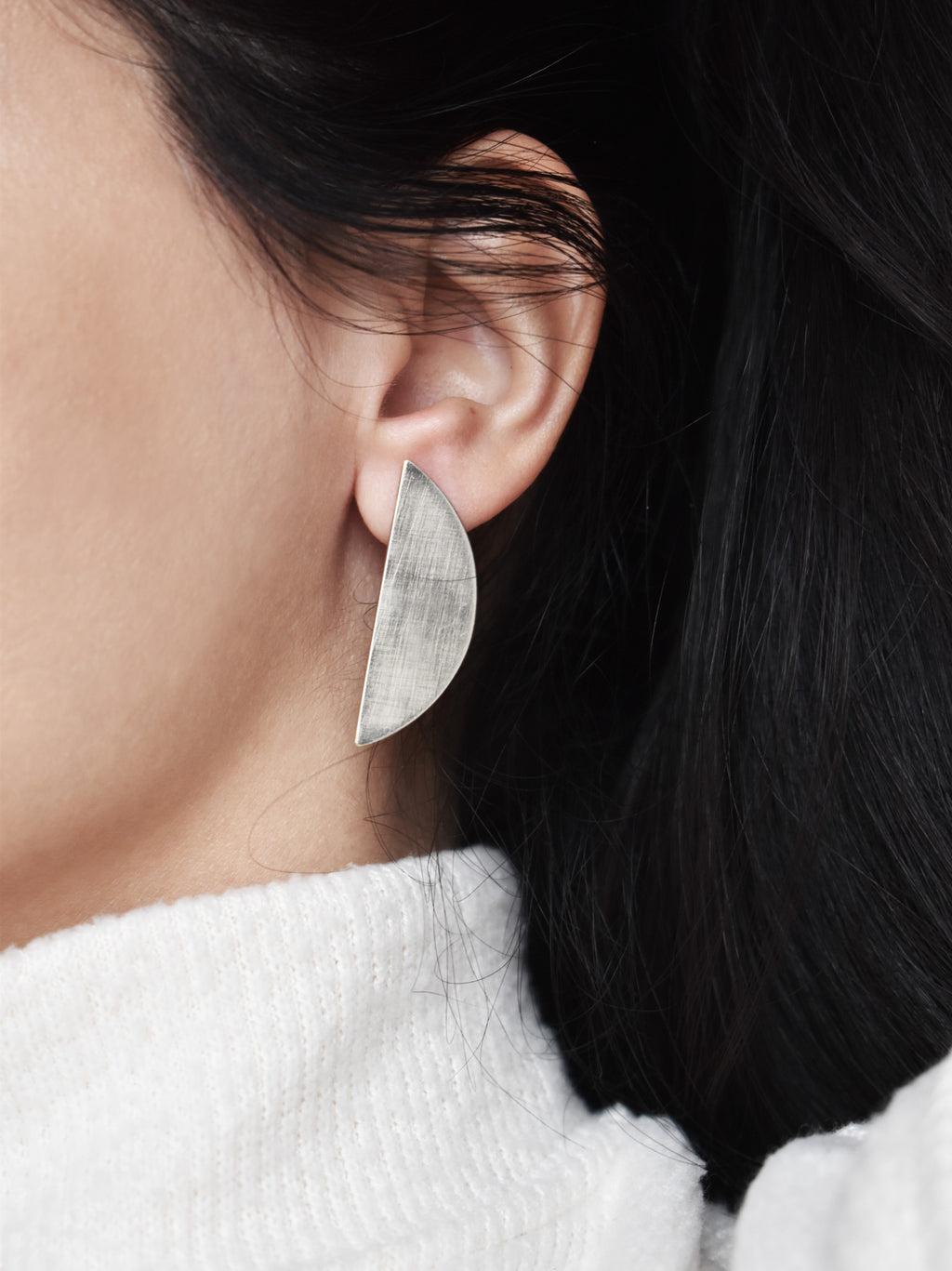 Close-up of a woman wearing a brushed silver semicircle stud earring