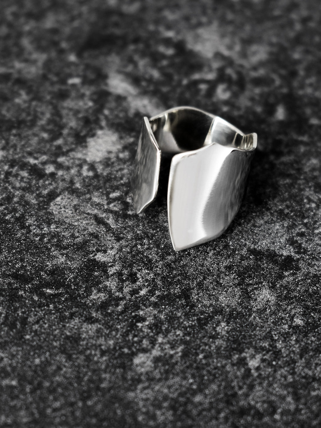 Adjustable sculptural silver ring on a dark textured surface