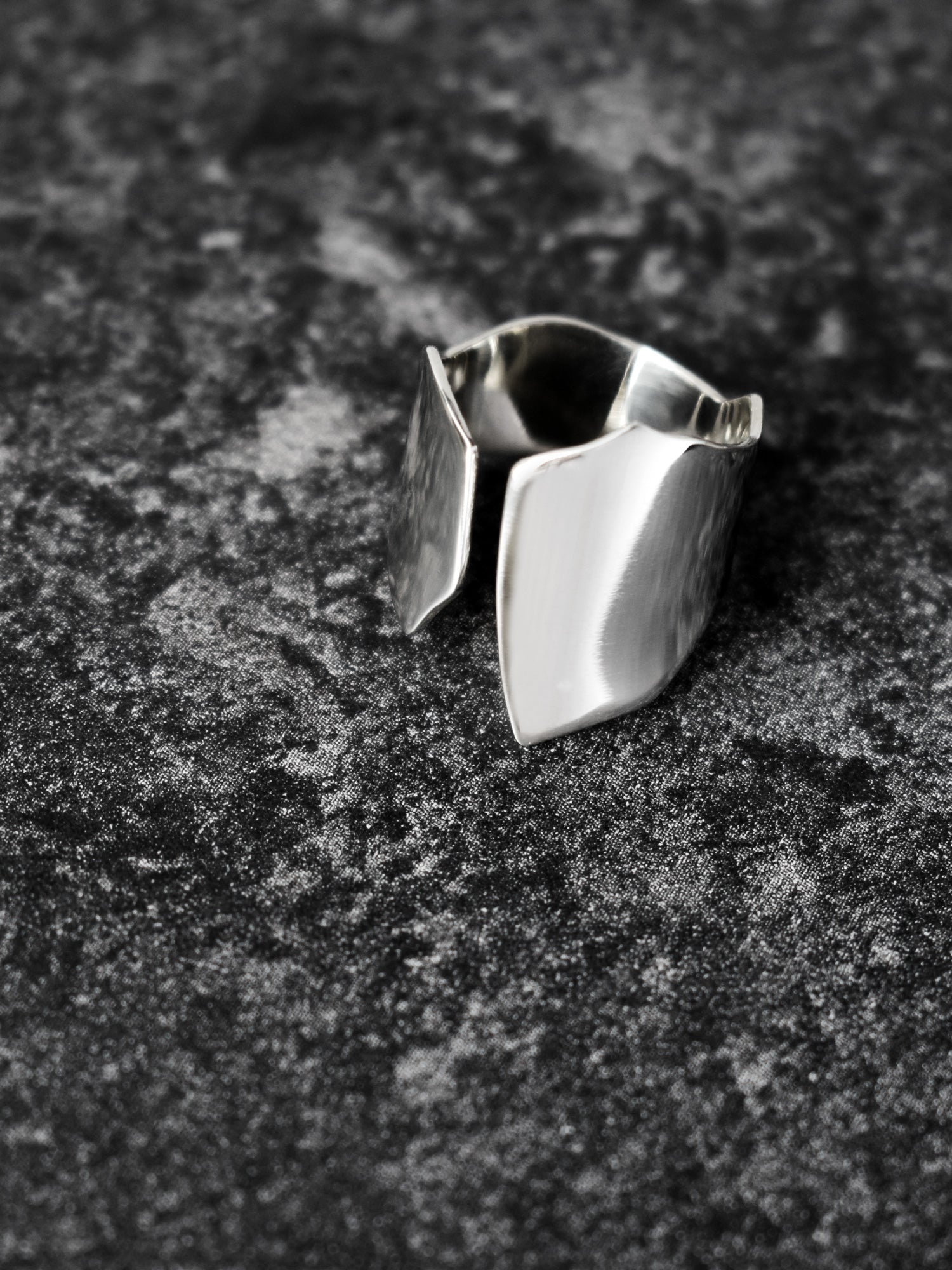 Adjustable sculptural silver ring on a dark textured surface