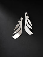 Pair of leaf-shaped silver stud earrings on a black background