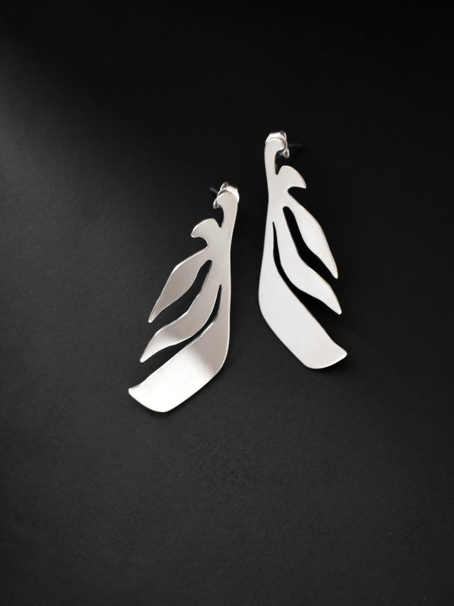 Pair of leaf-shaped silver stud earrings on a black background