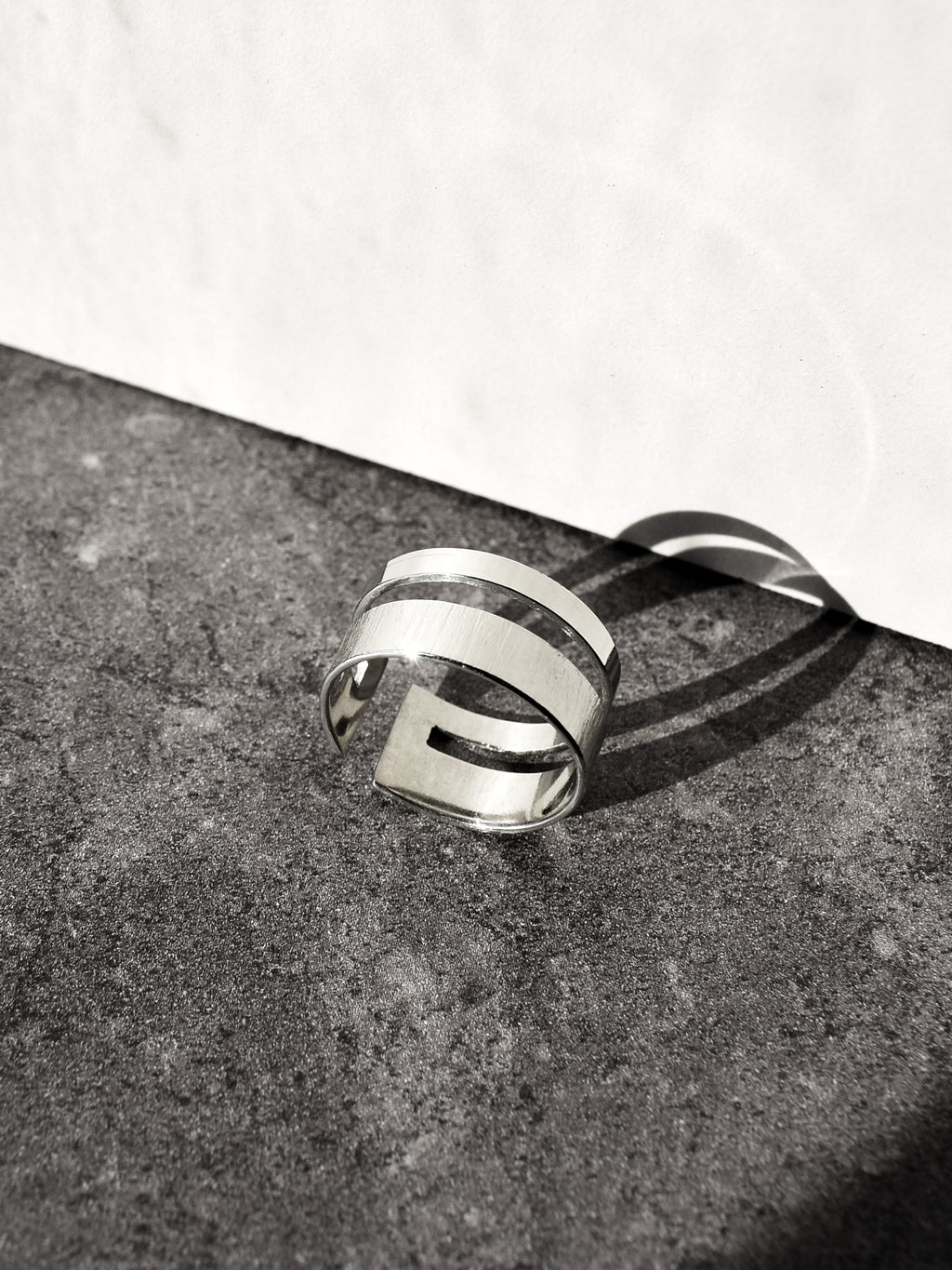 Adjustable double-band silver ring on a textured surface with a white background