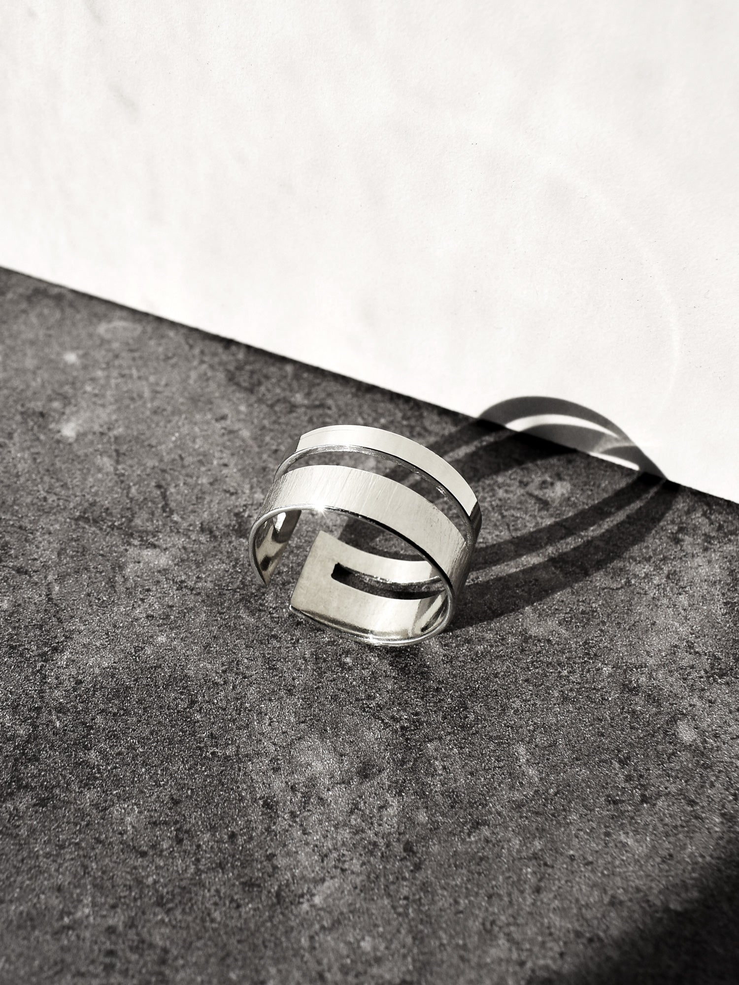 Adjustable double-band silver ring on a textured surface with a white background