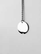 Small silver circle pendant with chain on a light gray background