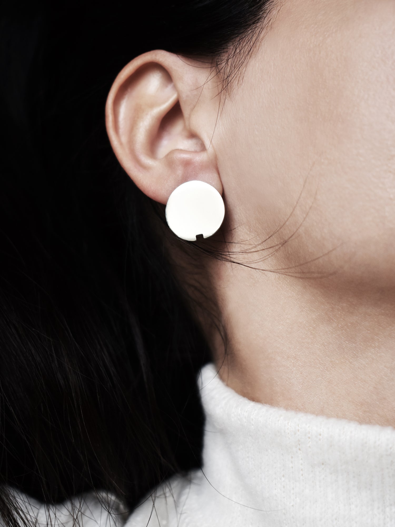 Close-up of a small circle silver stud earring worn by a woman