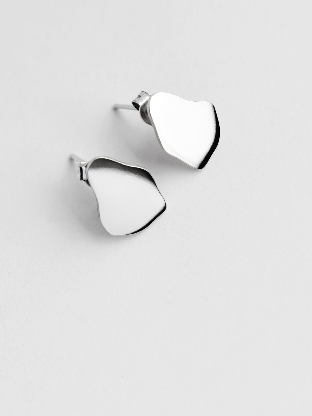 Pair of small organic-shaped silver stud earrings on a light gray background