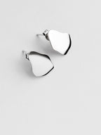 Pair of small organic-shaped silver stud earrings on a light gray background