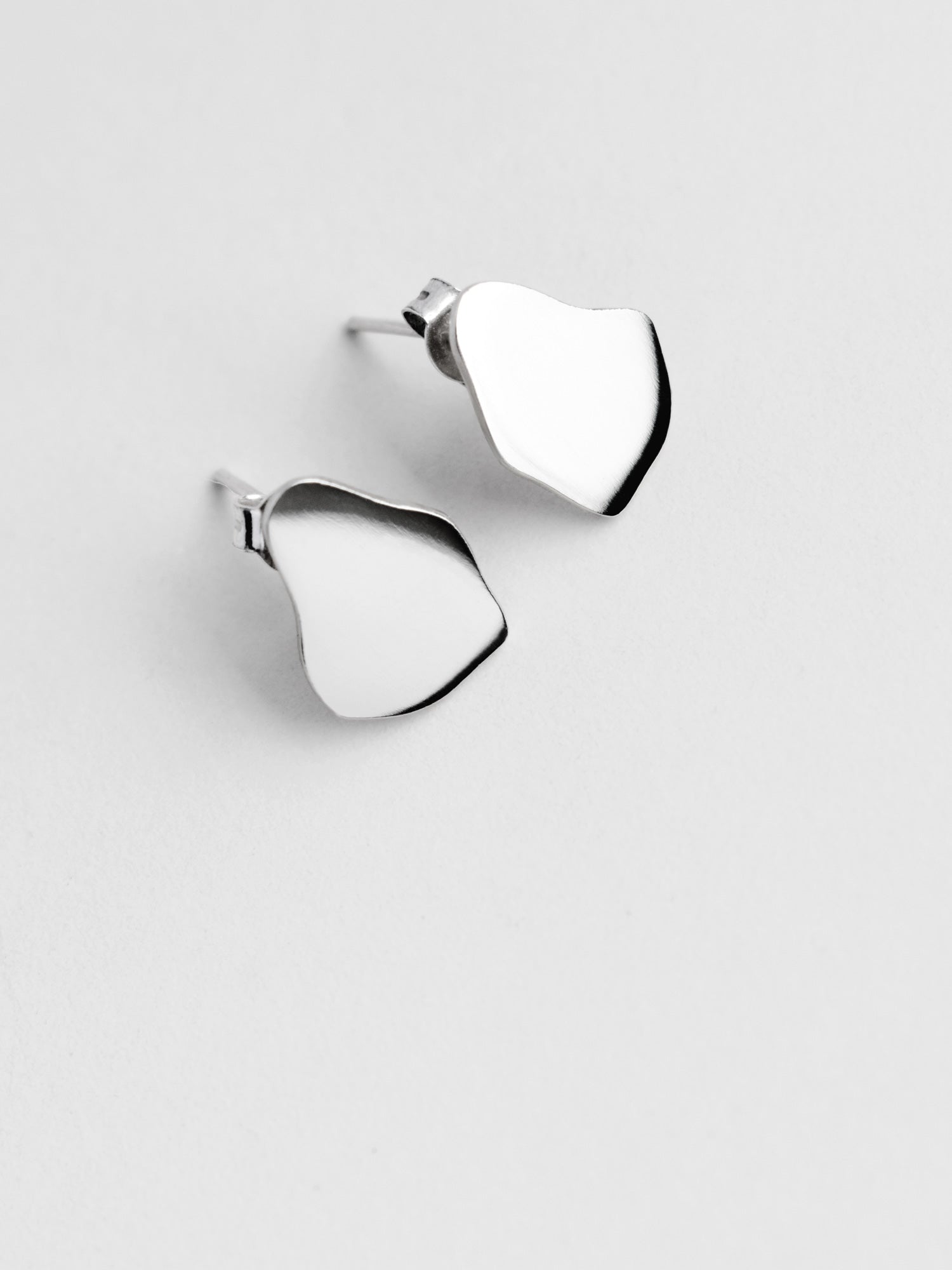 Pair of small organic-shaped silver stud earrings on a light gray background
