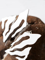 Close-up of pair of abstract-shaped silver stud earrings with flowing cutouts on a textured brown stone
