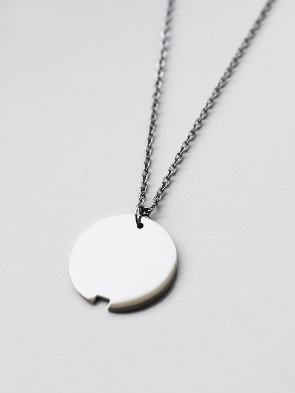 Close-up of small silver circle pendant with chain on a light gray background