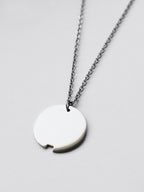 Close-up of small silver circle pendant with chain on a light gray background
