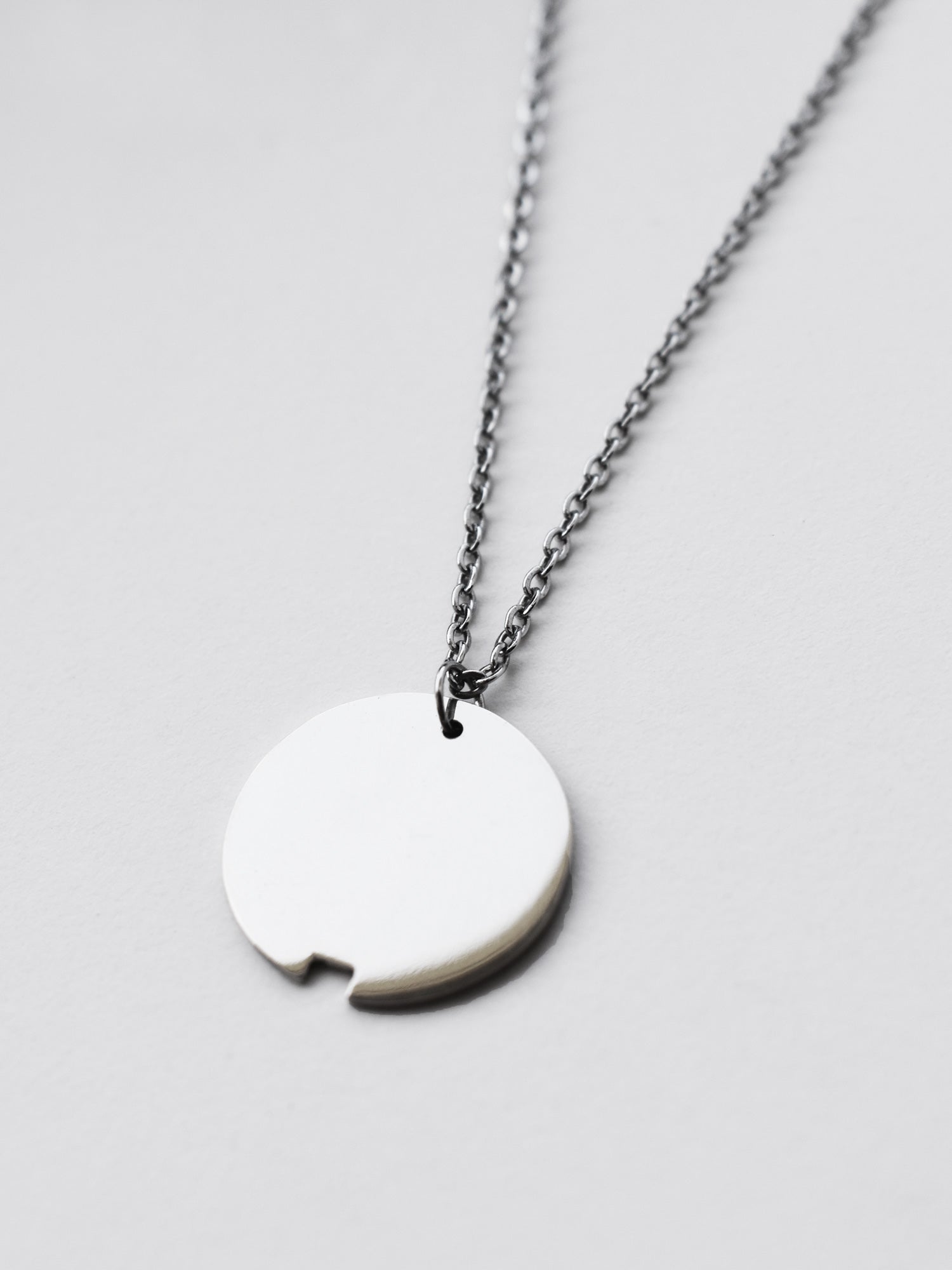 Close-up of small silver circle pendant with chain on a light gray background