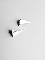 Pair of small curved triangular silver stud earrings on a light gray background