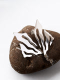 Pair of abstract-shaped silver stud earrings with flowing cutouts on a textured brown stone