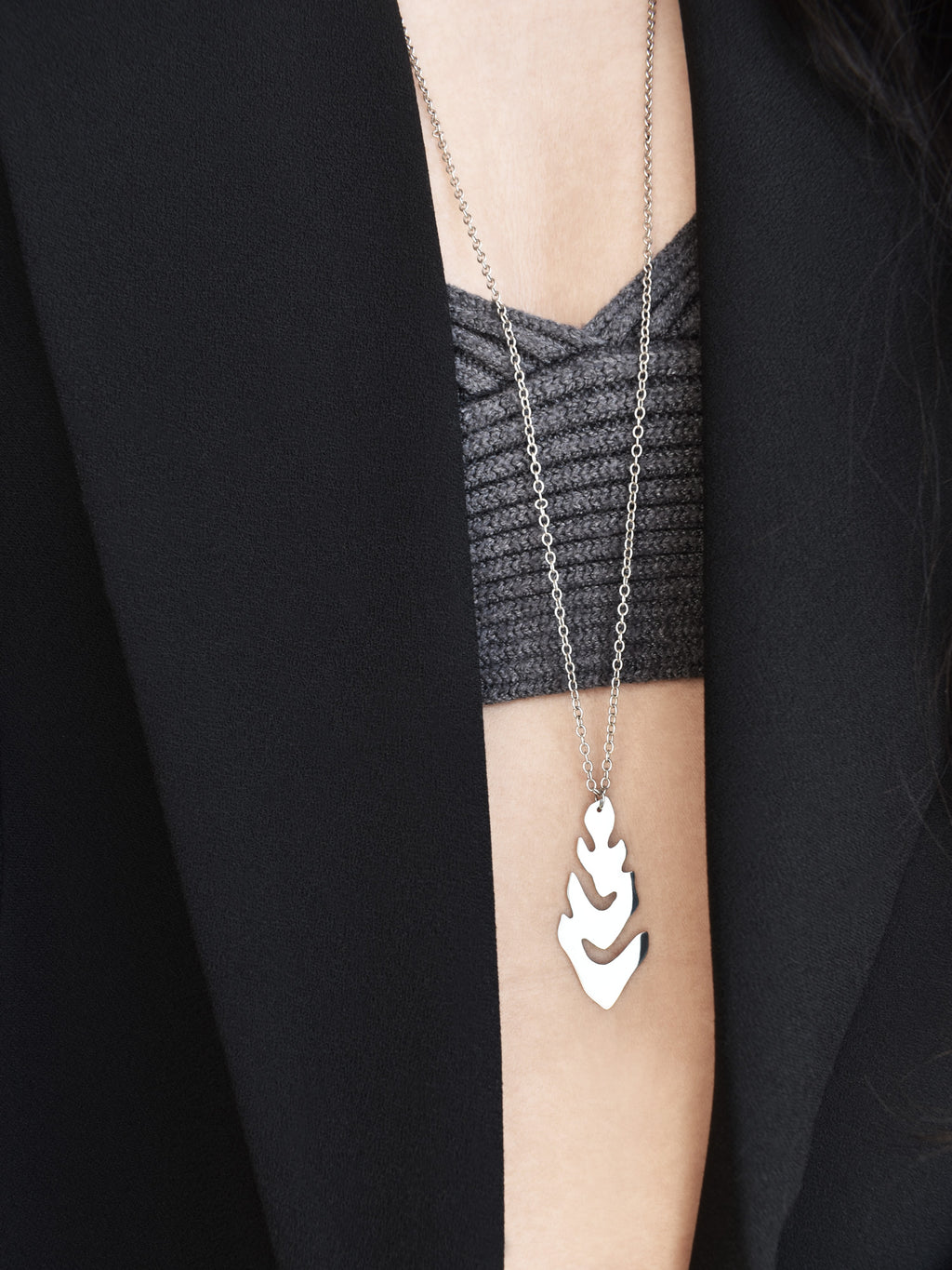 Silver leaf-shaped pendant with chain worn by a woman in a grey top and black blazer