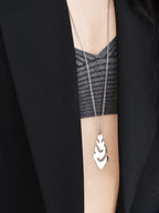Silver leaf-shaped pendant with chain worn by a woman in a grey top and black blazer