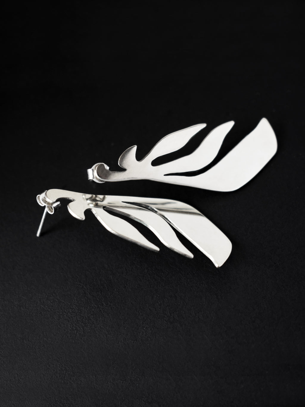Pair of leaf-shaped silver stud earrings on a black background