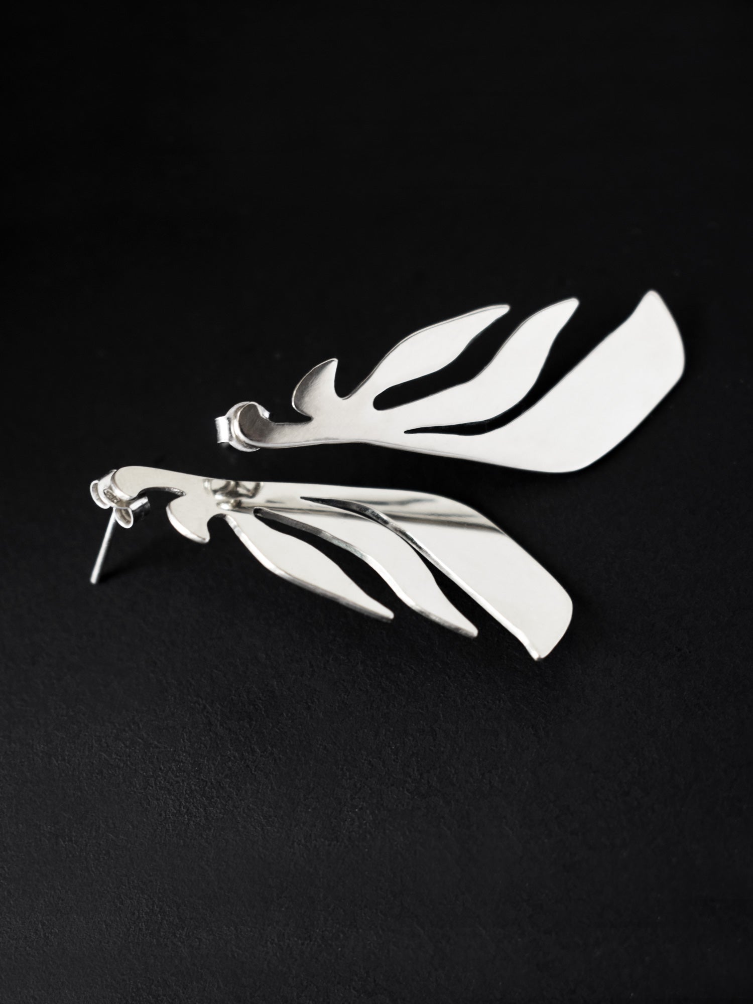 Pair of leaf-shaped silver stud earrings on a black background