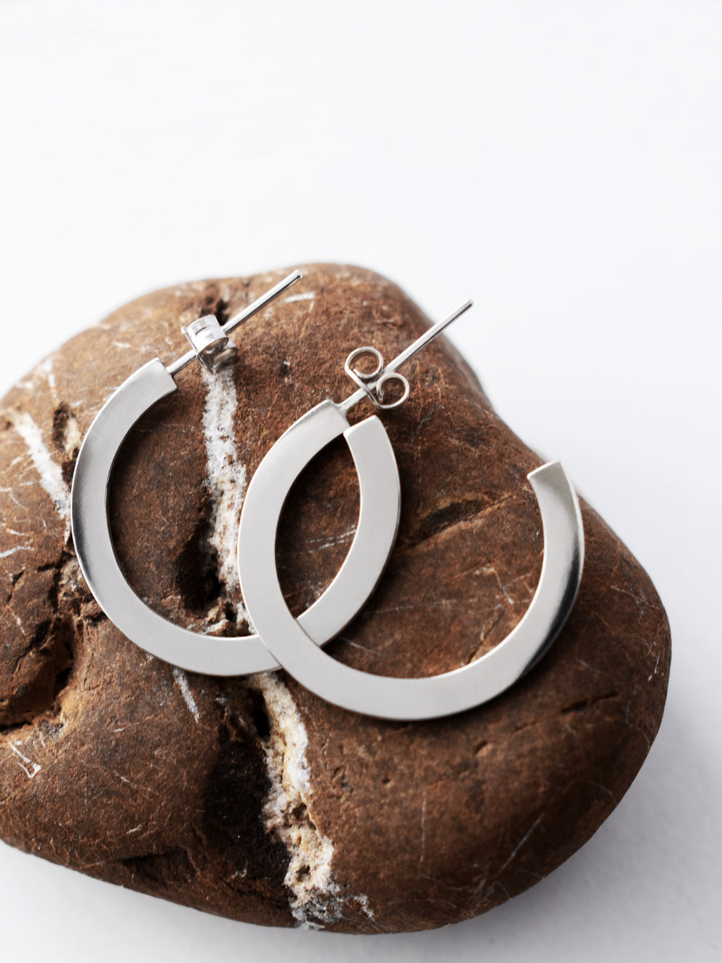 Pair of silver hoop earrings on a textured brown stone